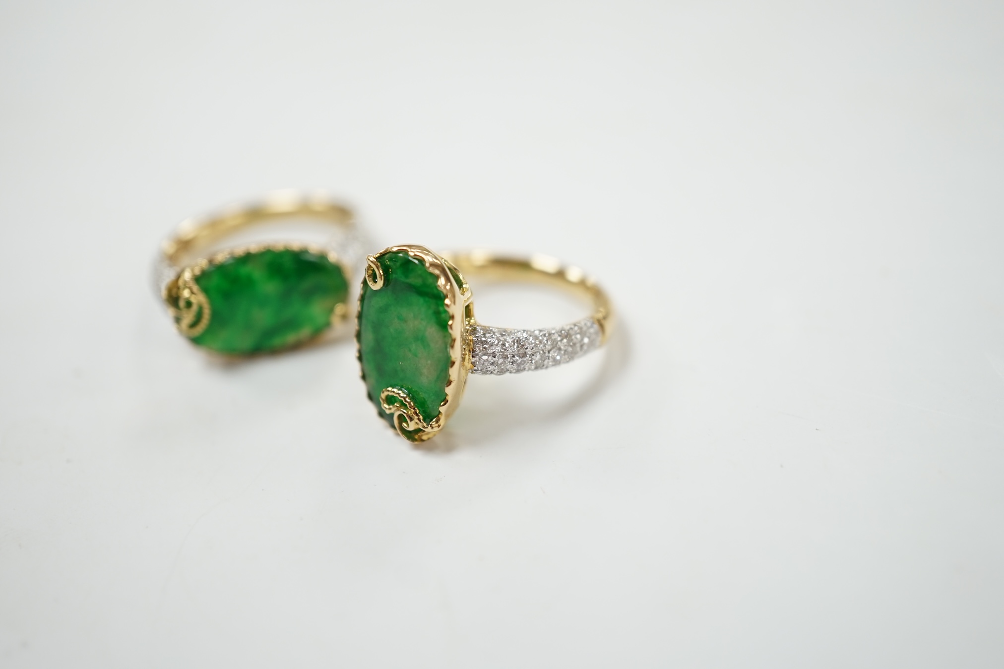 Two similar modern 18k and oval jade set dress rings, with diamond chip set shoulders, sizes K & L, gross weight 9.9 grams. Condition - good